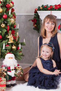 圣诞节或新年庆祝。幸福的母亲与她的女儿坐在附近的一棵圣诞树