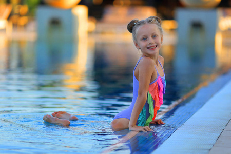 美丽的女孩在太阳镜在泳池度假在五颜六色的泳装