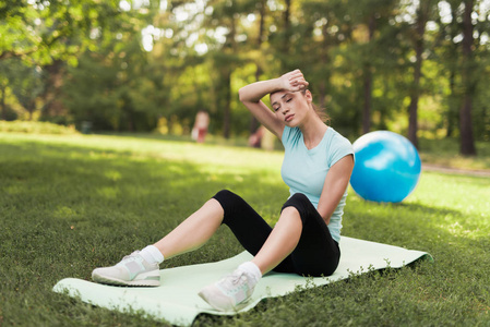 一个女人坐在地毯上做瑜伽, 锻炼后休息。她身后是一个蓝色的瑜伽球