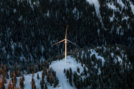 日落时在雪山顶上的风力涡轮机。