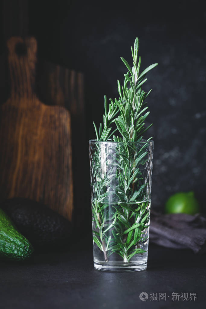 新鲜的迷迭香在玻璃与水在黑暗的背景