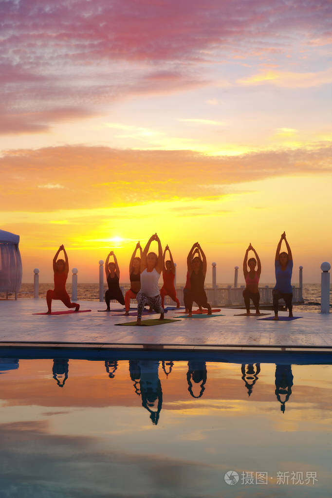 在海边日出时做瑜伽的一群妇女