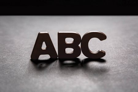 字母 Abc 的木制字母在黑暗的纹理与背光黑色背景。照明效果