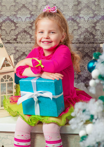 金发可爱的小女孩坐着微笑，几乎装饰圣诞树和新年礼物