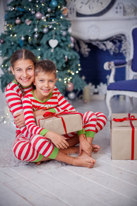 愉快的逗人喜爱的女孩和男孩穿着条纹睡衣坐在装饰的新年房间在家