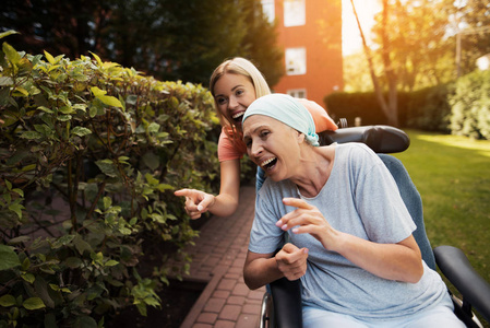 一位患癌症的妇女坐在轮椅上。她和女儿在街上散步, 他们玩得很开心。