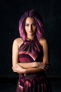 年轻美丽的女孩与粉红色卷曲的头发在黑暗的背景紫色礼服