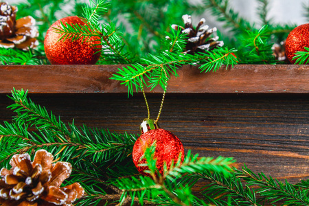 红色的圣诞球和球果躺在一个木褐色的架子上, 四周是冷杉树枝