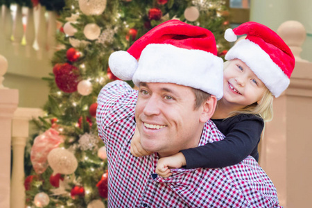 父亲和女儿在装饰圣诞树前戴着圣诞老人帽子