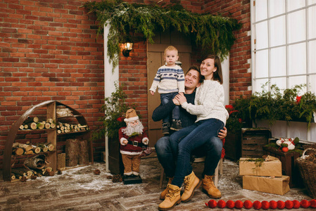 年轻快乐的父母带着一个可爱的小男孩穿着毛衣坐在椅子上与圣诞老人在装修的新年房在家里。圣诞节好心情。生活方式, 家庭和假日2018