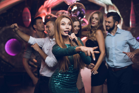 一个穿着绿色连衣裙的女人正在卡拉 ok 俱乐部和她的朋友们唱歌。她的朋友在背景上玩得很开心