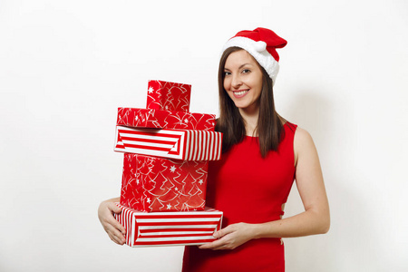 美丽的白种人年轻快乐的女人与迷人的笑容穿着红色的礼服和圣诞帽持有礼品盒白色背景。礼物被隔绝的圣诞老人女孩。新年假期2018概念