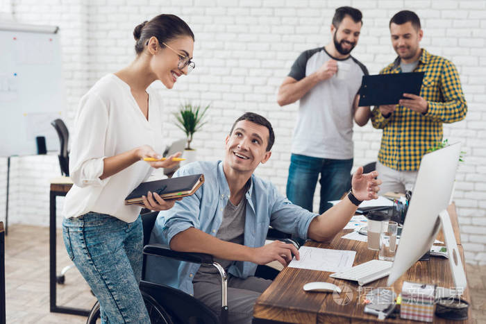 坐在轮椅上的男人正在和一个女孩谈话.他们在一个明亮的办公室工作