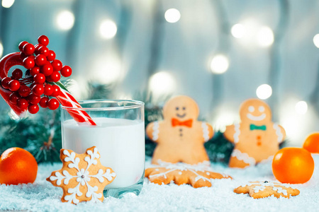 圣诞姜饼和牛奶配上装饰品, 雪, 圣诞树树枝上散模糊的灯光背景。自由空间