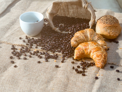 咖啡豆在粗麻布袋子与杯子和羊角面包