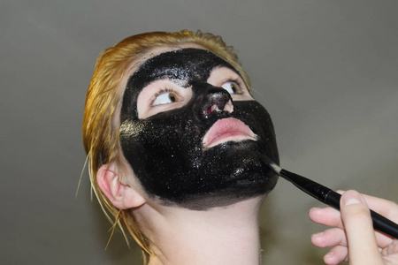 戴着黑色化妆面具的女孩。阿司匹林和活性炭的洁面面膜。黑色化妆面膜
