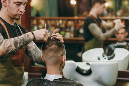 近距离拍摄的人在理发店流行发型。男性发型师在纹身服务客户