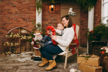 可爱的年轻快乐的母亲与逗人喜爱的小男孩穿着毛衣坐在椅子上与圣诞老人在装饰的新年房间在家。圣诞节好心情。生活方式, 家庭和假日20