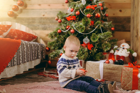 快乐可爱的小男孩穿着毛衣和牛仔裤装饰圣诞树与玩具在家里的木制房间。有好心情的孩子。新年。生活方式, 家庭和假日2018概念