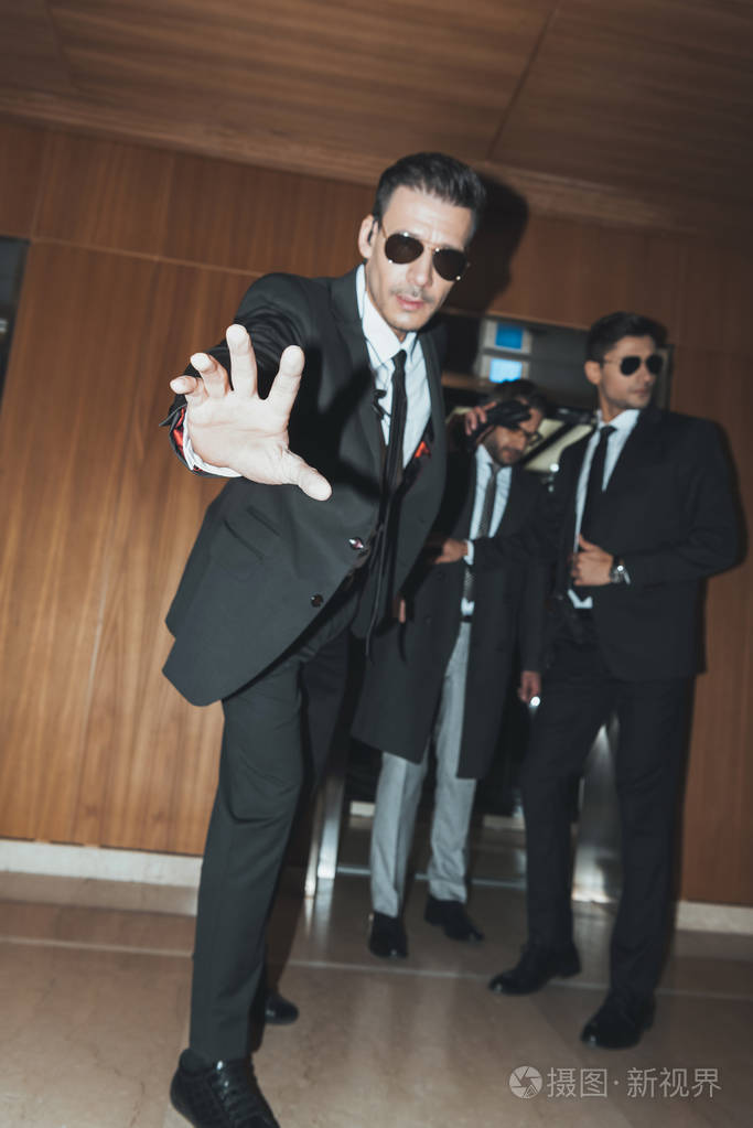 戴墨镜的保镖当名人从电梯里出来的时候阻止狗仔队