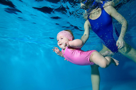 一个小女孩在游泳池里水下游泳，妈妈。 肖像。 底部视图从水下。 景观定位