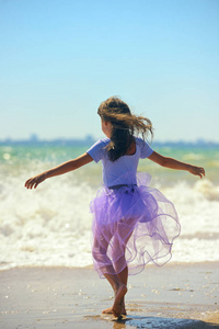可爱的小女孩在海边跳舞，手臂伸出，穿着一条发展的裙子。肖像导向