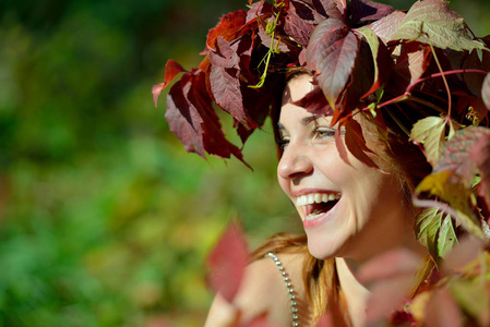 阳光明媚的一天，戴着红色和绿色叶子花环的快乐女孩在绿色背景上欢快地笑着