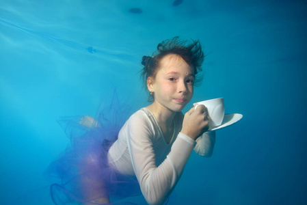 快乐的小女孩在水下游泳,拿着白色的杯子和碟子看着我.