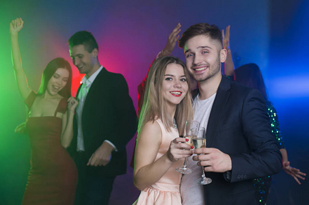 一群年轻开朗快乐的朋友正在聚会上跳舞。 一男一女在前台跳舞，拿着香槟碰杯