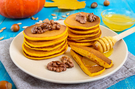 芬芳的金色南瓜煎饼，蜂蜜和核桃在蓝色的木制背景上。 传统美式菜肴