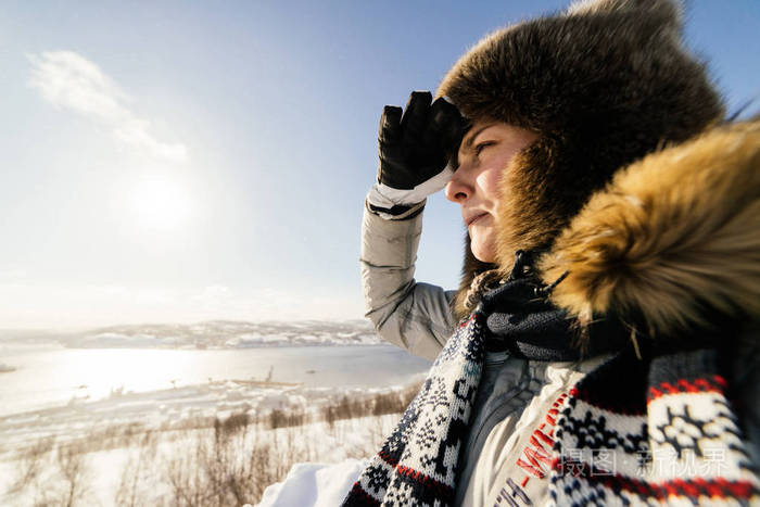一个穿着毛皮帽子的年轻女孩穿着暖和的衣服望着远方在寒冷的冬天里在