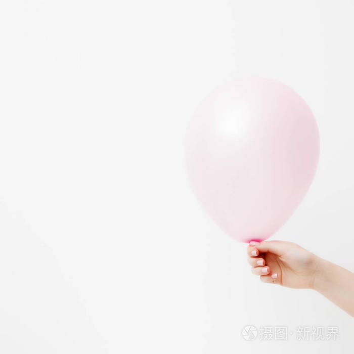 简约时尚和美丽的照片。手拿着一个粉红色的气球在白色的墙壁背景与阴影反射。St. 情人节或生日的概念。2月14日