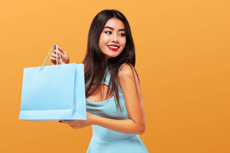 购物节。愉快的亚洲妇女在购物手提袋和电话隔绝在蓝色背景在黑色星期五假日。销售广告的复制空间