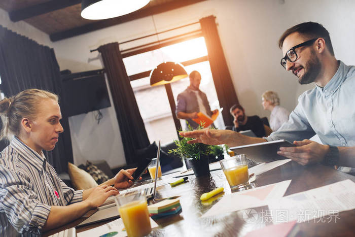 两个现代的年轻商人围坐在桌旁, 在笔记本电脑和平板计算机上工作.