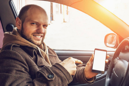 年轻的司机在他的汽车手持智能手机或手机与空白的白色屏幕模拟或空白为您的产品