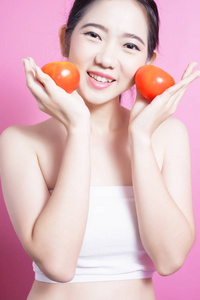 亚洲妇女与蕃茄概念。她微笑着捧着西红柿。美丽的脸庞和自然的妆容。在粉红色背景上隔离