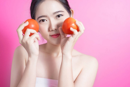 亚洲妇女与蕃茄概念。她微笑着捧着西红柿。美丽的脸庞和自然的妆容。在粉红色背景上隔离