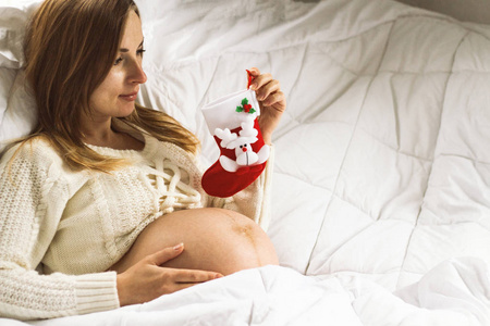 怀孕的年轻女孩拿着一只圣诞袜子, 看着他