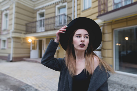 一个人的女孩在美丽的旧建筑周围摆了一架照相机。一个时髦的女人在一个黄色的房子的背景下的晚上肖像