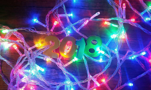 新年和圣诞闪烁的花环和数字2018在黑色的木制背景灯