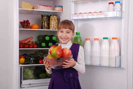 美丽的女孩在冰箱附近与健康食物