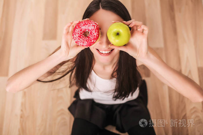 饮食。年轻的女子捧着一份披萨的尺度和使一个苹果和一个甜甜圈之间的选择。健康饮食的概念
