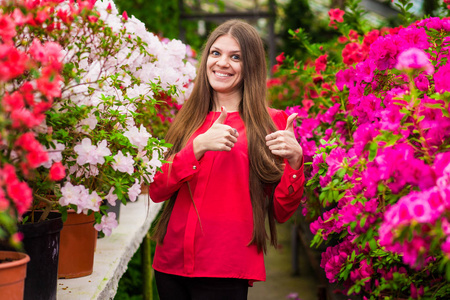 站在玫瑰花园里的年轻笑妇穿着一件红色上衣竖起大拇指