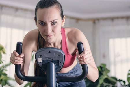 欧洲妇女训练有氧健身运动在家里锻炼自行车。减肥的概念。有上进心和专注的年轻女孩