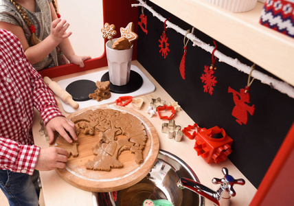 孩子们做圣诞曲奇饼.男孩切饼干面团在木板在设计师玩具厨房照片