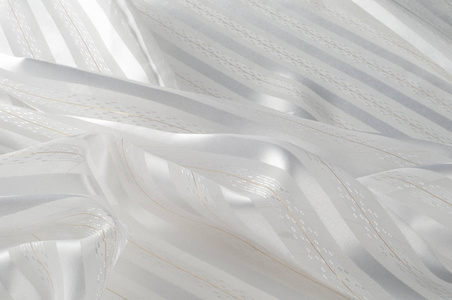 背景纹理图案。 白色丝绸织物，带轻条。 波纹白色丝绸织物的特写。 光滑优雅的金丝可用作婚礼背景。 复古风格