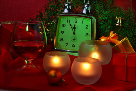 圣诞钟, 玻璃杯干邑或威士忌和蜡烛。新的岁月装饰与礼物箱子圣诞节球和树。新年庆典概念