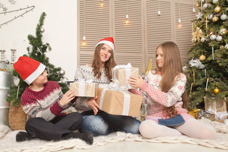 一个真正的家庭，母亲，女儿和儿子，都很快乐，在圣诞树附近度过一段美好的时光，并在房间里赠送礼物