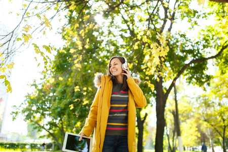 在一个温暖的日子里, 一个穿着黄色外套, 条纹 longsleeve 的美丽快乐的棕色头发的女人, 在秋天的城市公园里, 手里拿