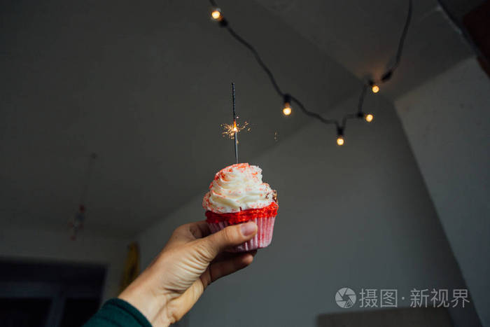 女人的手拿着粉红色的纸杯蛋糕上面有糖霜和鲜奶油贴在房间的墙壁上